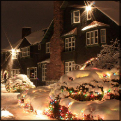 A large and beautiful house, lit up by Christmas lights in the snow at night.