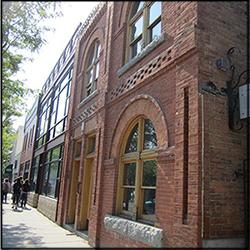 An angled color photo of a brick building with decorative brick on its face and large windows.