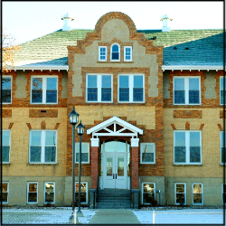 A color photo of a two floor, brown and tan, brick building which features brick decoration on its face.