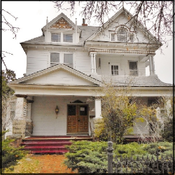A color photo of a three story white townhouse in the fall.