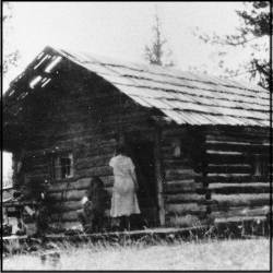 A high contrast black and white photo of a log cabin.
