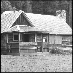 A black and white photo of a log cabin with a stone chimney.