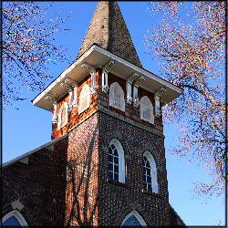 A color photo zoomed in on the bell tower of a brick church.