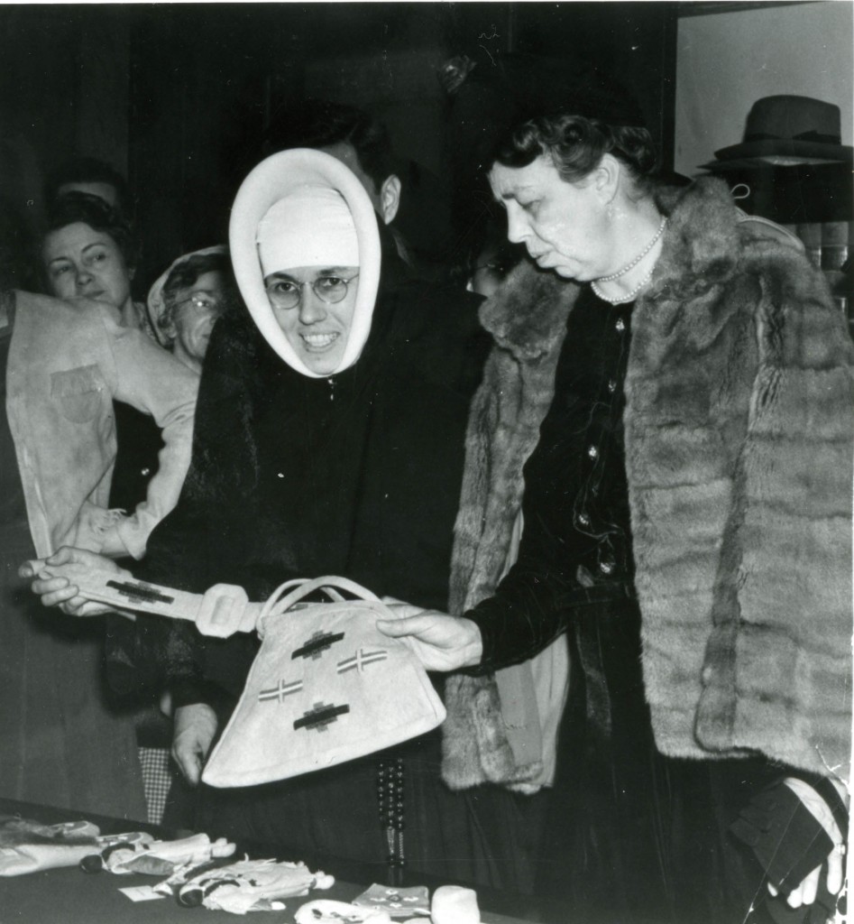 Sister Providencia, in full habit, with Eleanor Roosevelt, in a fur cape, admiring a decorated bag.